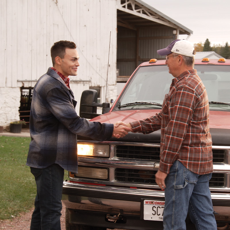 Michael Alfonso shaking hands with a farmer near a red truck