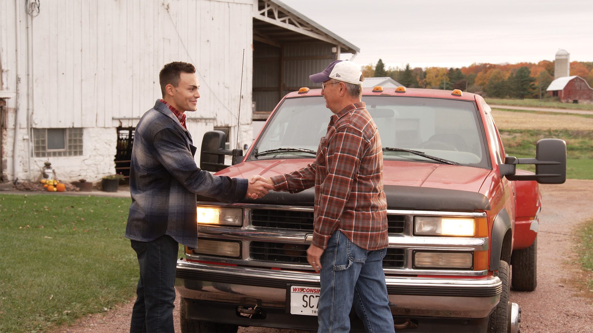 Michael Alfonso shaking hands with a farmer near a red truck